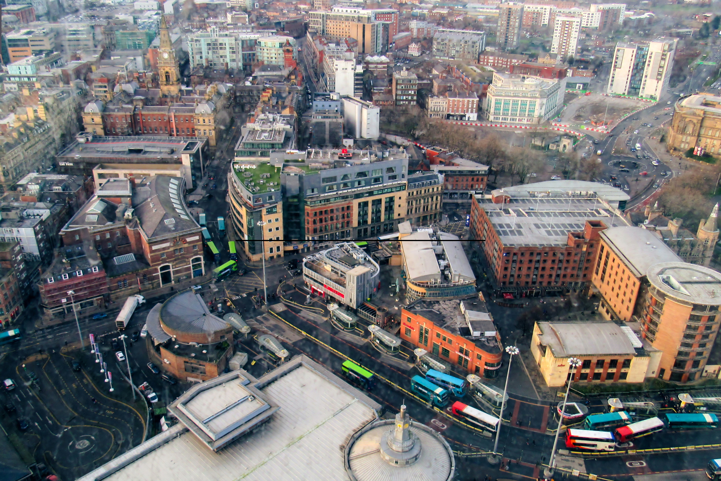Aerial view of urban landscape in Leeds featuring buildings, roads, and multiple buses, illustrating the city's infrastructure and vibrant construction environment.