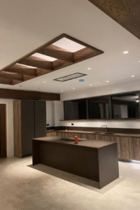 Modern kitchen interior featuring a central island, wooden cabinetry, recessed lighting, and large mirrors, showcasing Solved Construction's renovation expertise.