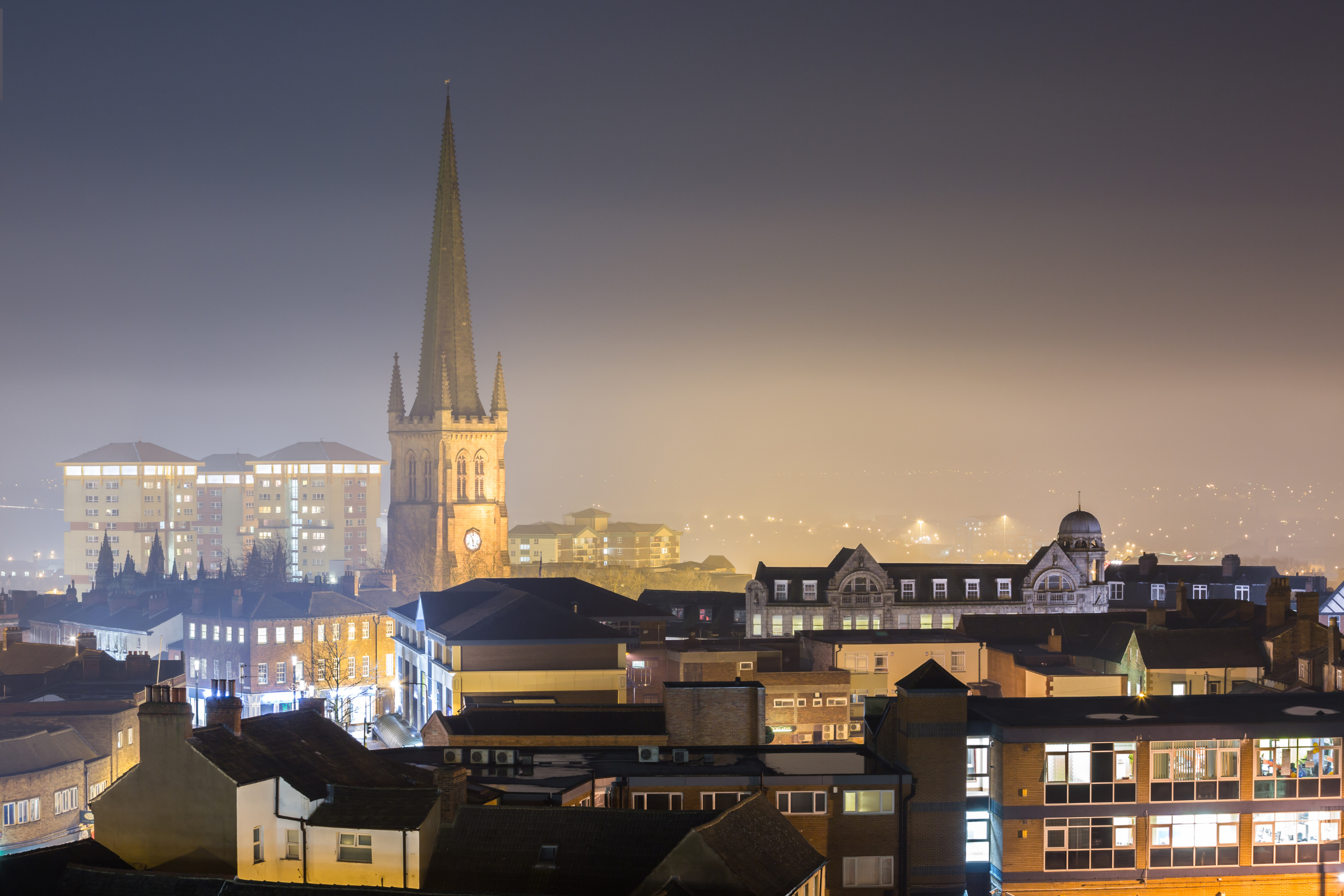 Nighttime view of Wakefield cityscape featuring the prominent clock tower, illuminated buildings, and a misty atmosphere, reflecting the local architecture and urban landscape relevant to Solved Construction's service area.